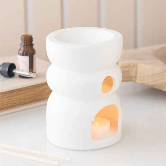 White ceramic oil burner with a small candle inside on a light surface.