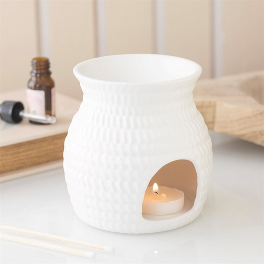 White ceramic oil burner with a lit candle inside on a light surface.