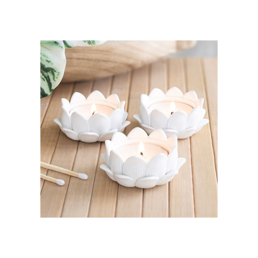 Three white lotus-shaped candle holders with candles on a wooden surface.
