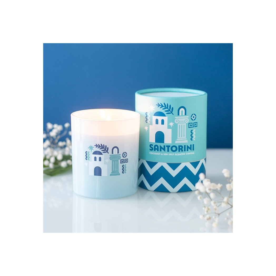 Candle and decorative container with Santorini design on a white surface with blue background