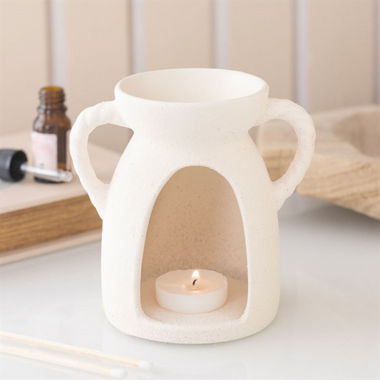 White ceramic oil burner with a lit candle inside on a neutral background
