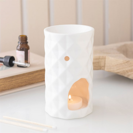 White ceramic oil burner with a small candle inside on a light wooden surface.